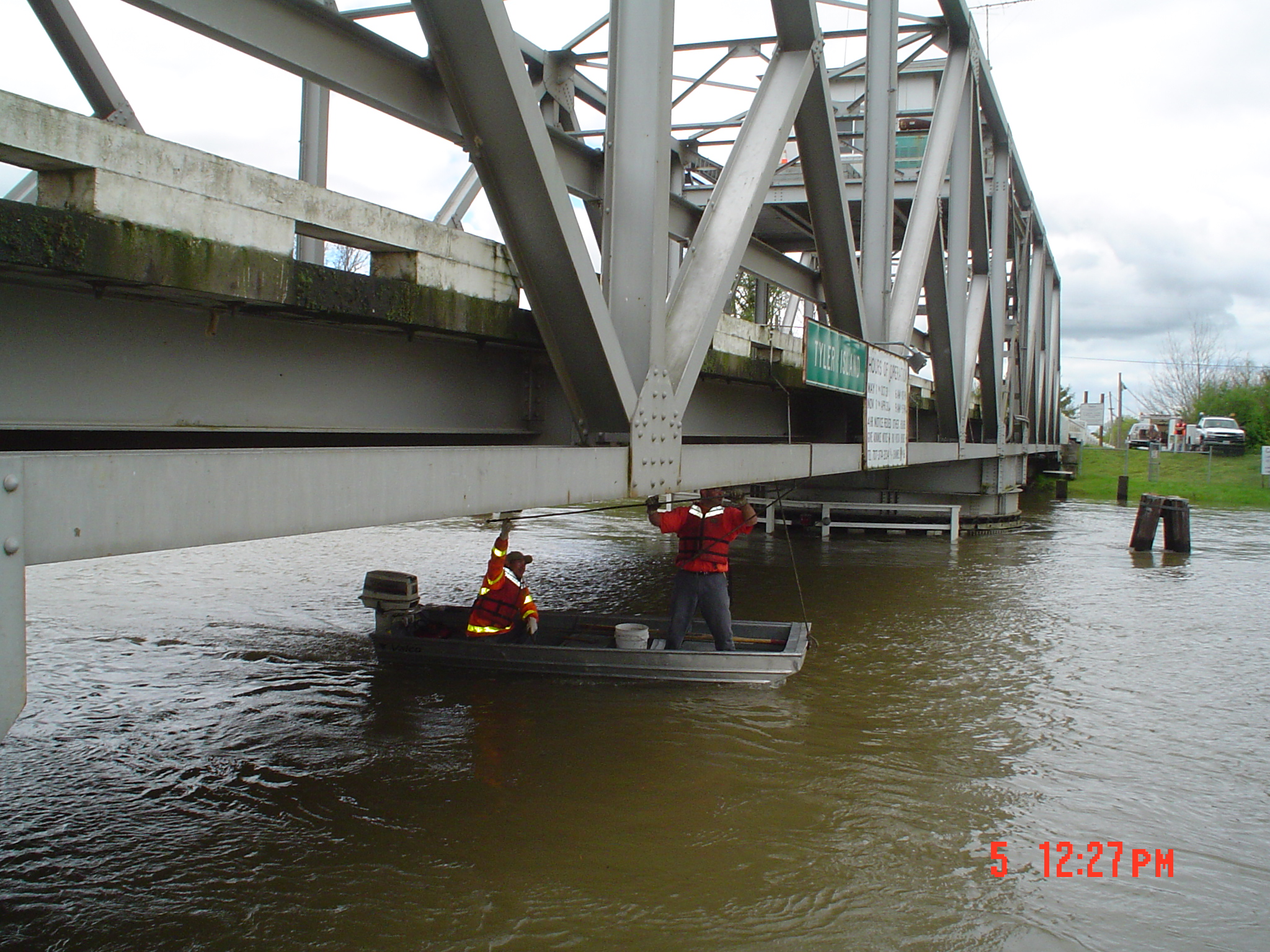 Maintenance workers performing repairs on the Tyler Island Road Bridge, using a small boat to go underneath the bridge.
